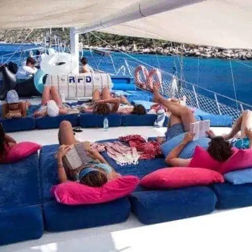 A group of people relaxing on a catamaran with blue cushions, enjoying a sunny day on the sea.