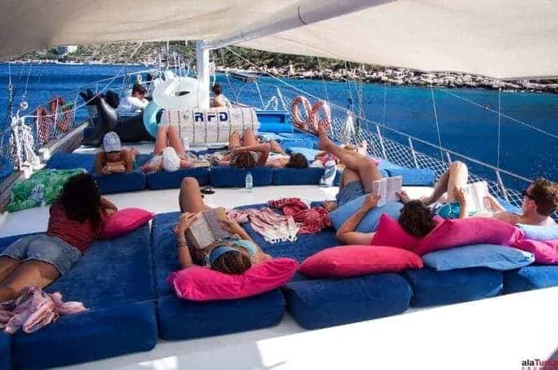 A group of people relaxing on a catamaran with blue cushions, enjoying a sunny day on the sea.