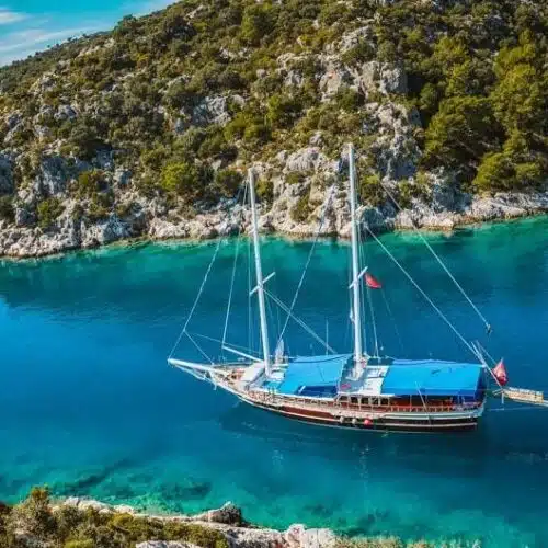 A sailboat is anchored near a rocky coastline with clear turquoise waters.