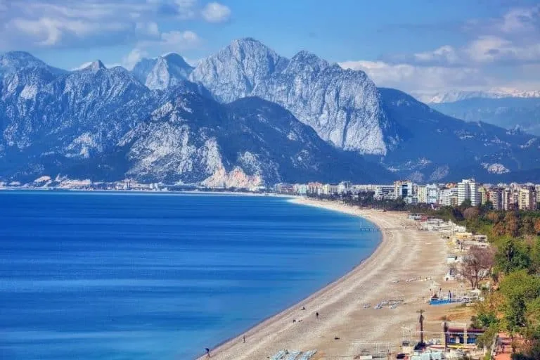 Panoramic view of the Antalya coastline featuring the calm sea and distant mountains under a bright sky.