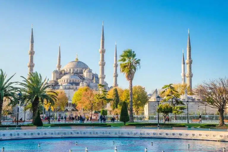 Exterior view of the Blue Mosque in Istanbul, showcasing its grand domes and six slender minarets against a clear sky.