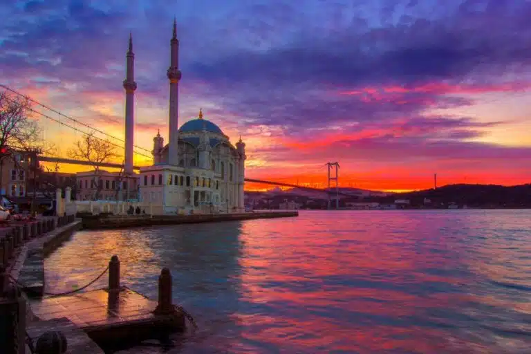 Ortakoy Mosque and Bosphorus Bridge at sunset with orange sky backdrop.