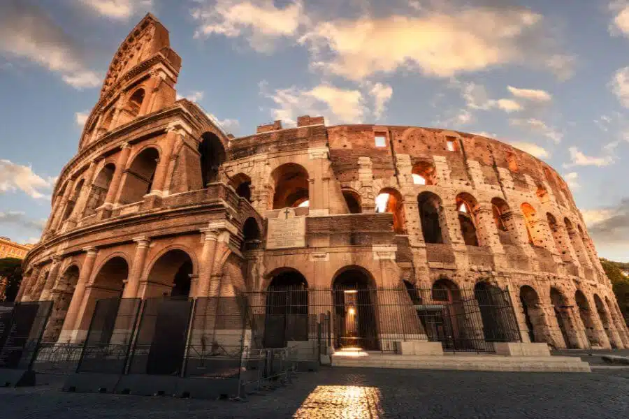 Exterior view of the ancient Colosseum in Rome, Italy, showcasing its iconic arches and historic architecture under a clear sky.