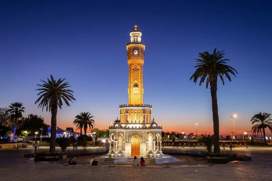 Konak Clock Tower at sunset in Konak Square, Izmir, with the tower's intricate design silhouetted against the vibrant sky.